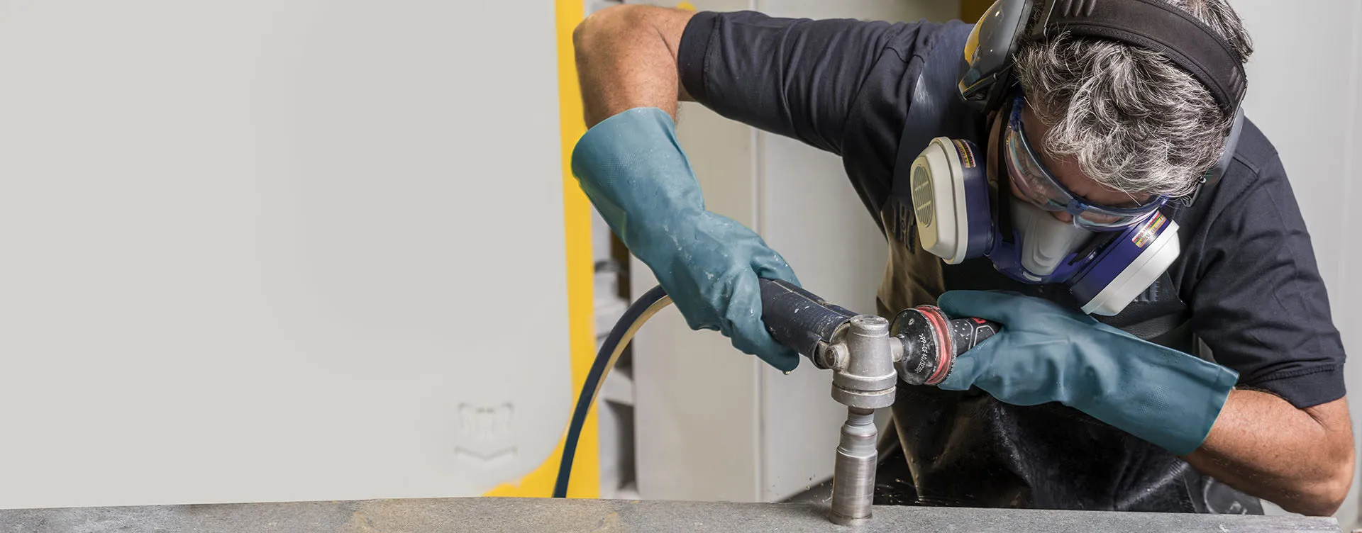 Fabricator polishing a Caesarstone surface using a power tool, wearing protective gloves, mask, and ear protection.