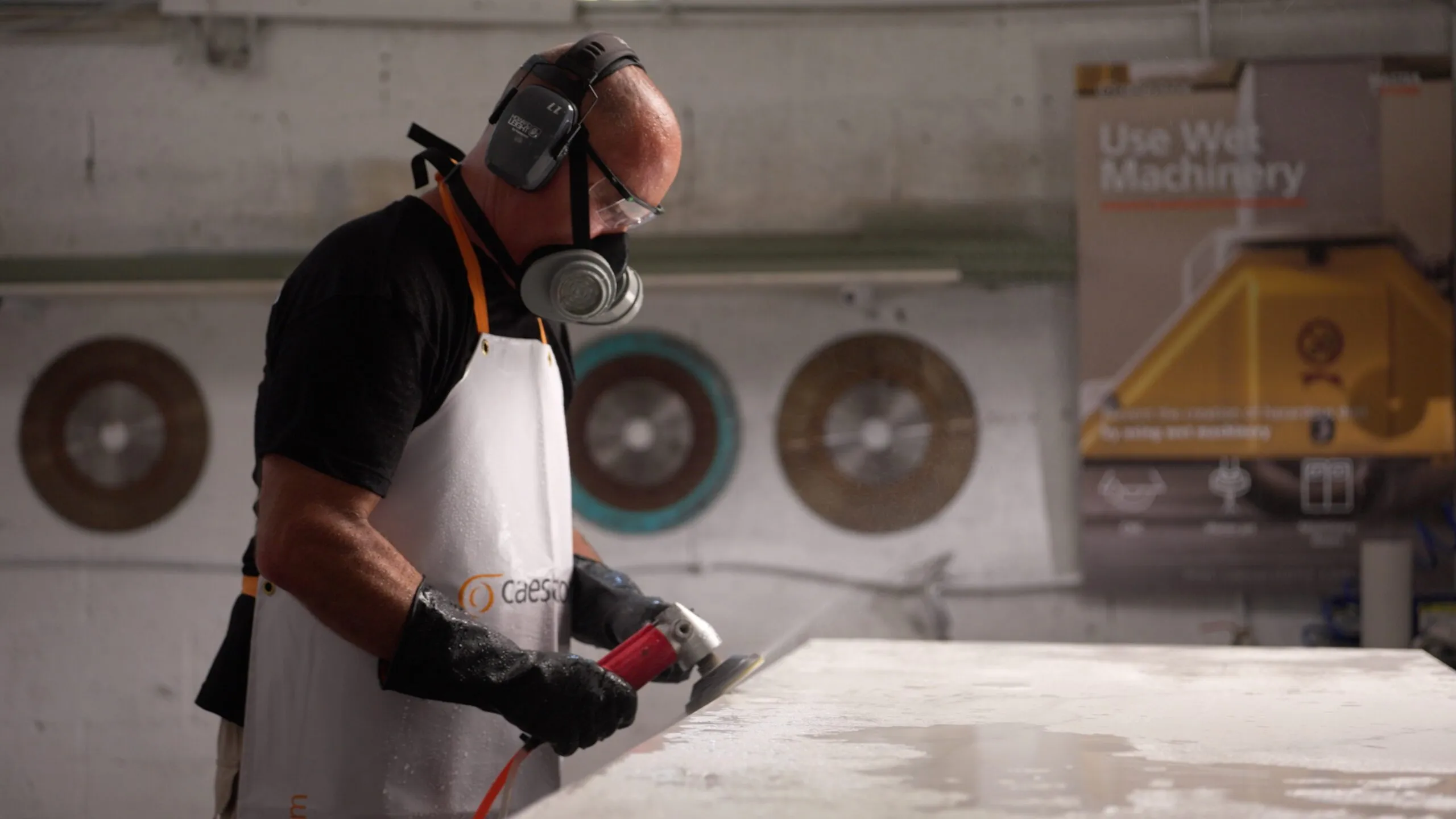 A worker wearing protective gear polishes or grinds a Caesarstone Porcelain surface in an industrial setting.